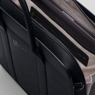 Close-up of a black laptop bag with the zipper open, revealing a soft light-colored interior, padded laptop compartment, inner zip pocket, and room for work essentials.