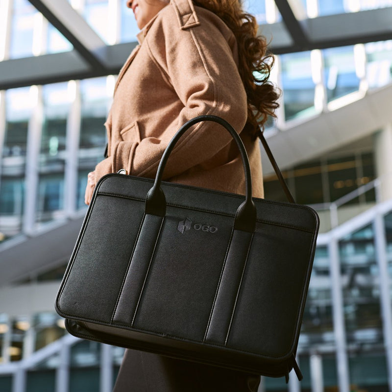 Close-up lifestyle image of a woman carrying a black laptop bag over the shoulder, highlighting the structured shape, top handles, and polished work bag design.