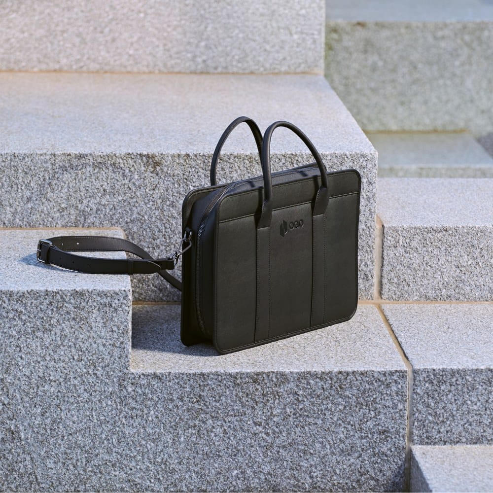 Black laptop bag placed on stone steps outdoors, featuring a detachable shoulder strap, slim briefcase silhouette, and refined style for commuting, work, or travel.