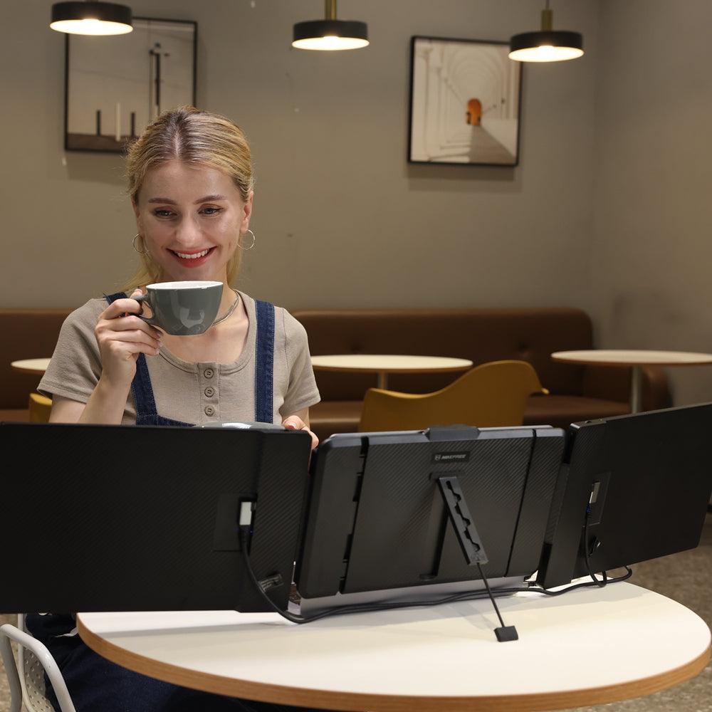 Woman working at a café using a 14.1-inch triple screen portable monitor setup attached to her laptop, sipping coffee while multitasking on multiple extended displays