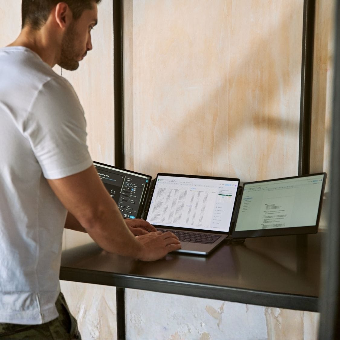 Person working at a desk with a laptop and two portable monitor screens displaying separate applications in a three-screen workspace.