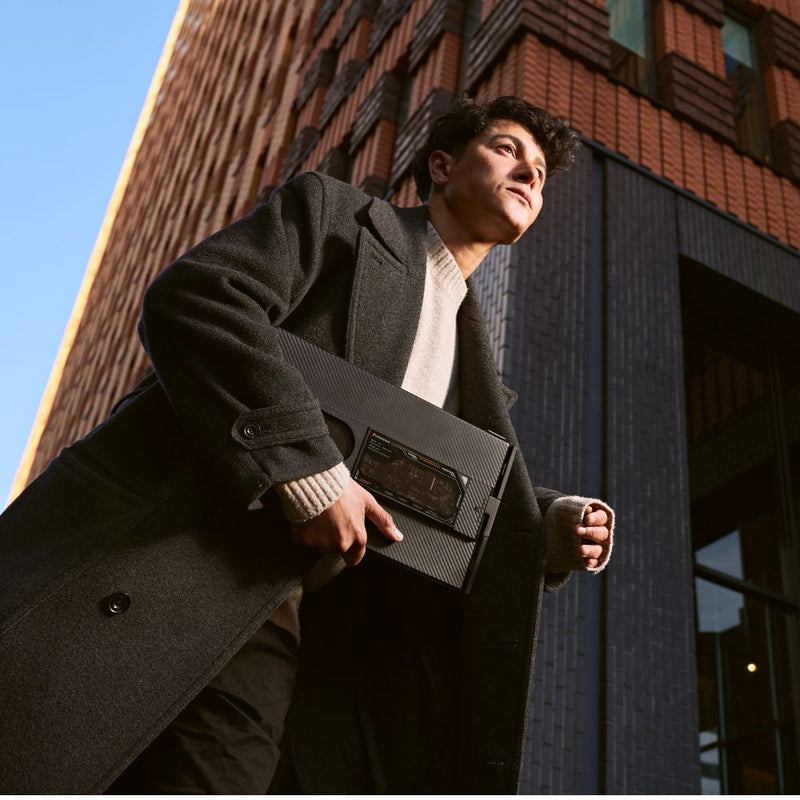 Person walking outdoors with a folded portable monitor tucked under one arm, highlighting the compact, travel-friendly design of the 15.6-inch dual-screen display.