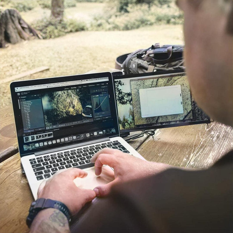 Person using a portable monitor dual screen setup outdoors, editing photos on a laptop with an extended display for multitasking