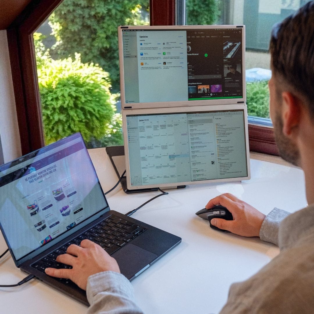 Person working at a desk using a portable monitor triple-screen setup, with two side screens extending from a laptop for multitasking