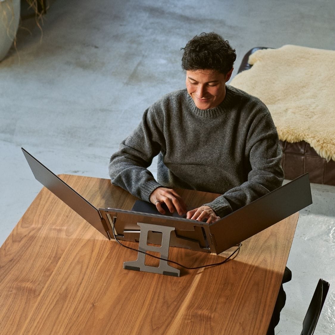 Person working at a wooden table with a portable monitor extended on both sides of a laptop for a spacious three-screen workstation.