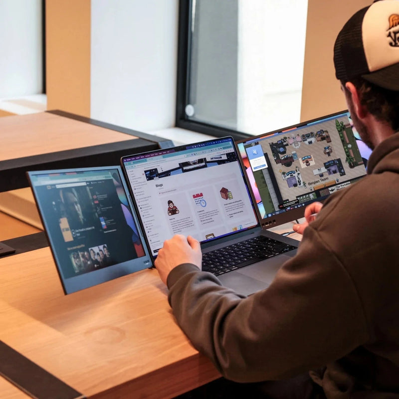 Man working at a desk using a 15.6-inch triple screen portable monitor setup, with three extended displays open for productivity and collaboration