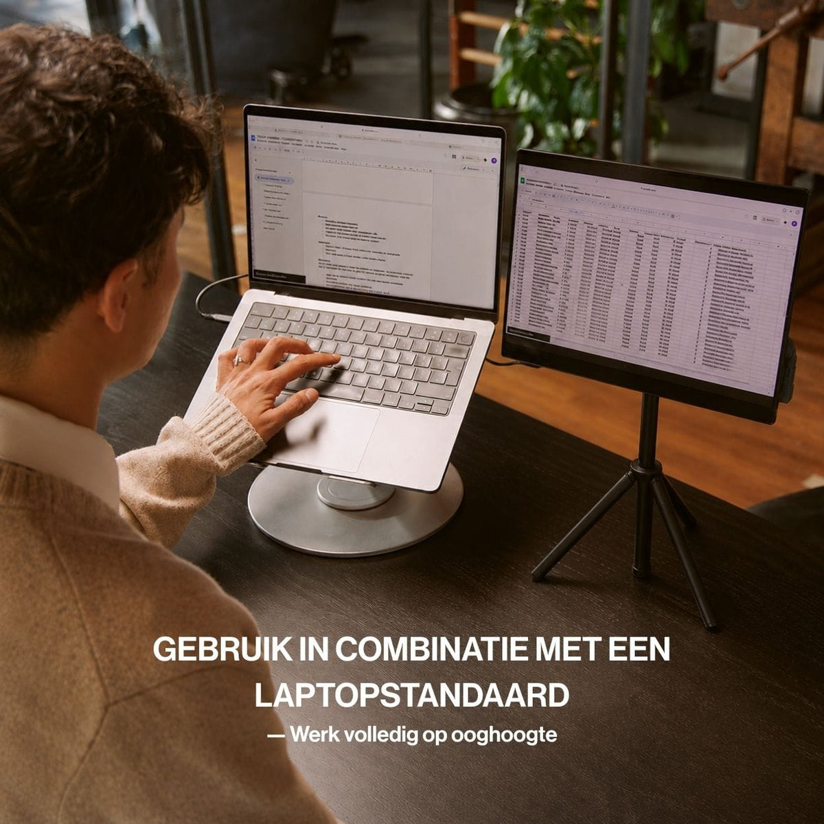 Portable monitor op een driepoot naast een verhoogde laptop voor een ergonomische werkplek met twee schermen op ooghoogte.