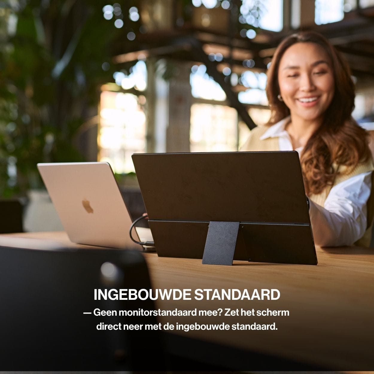 OneSight AMOLED portable monitor positioned beside a laptop using its integrated kickstand, allowing the screen to stand securely without a separate monitor stand.